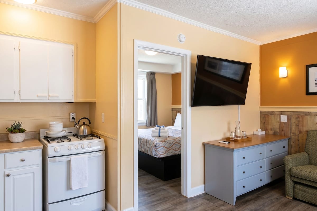 A compact hotel room with a kitchenette, a bed, a TV, and a small seating area.