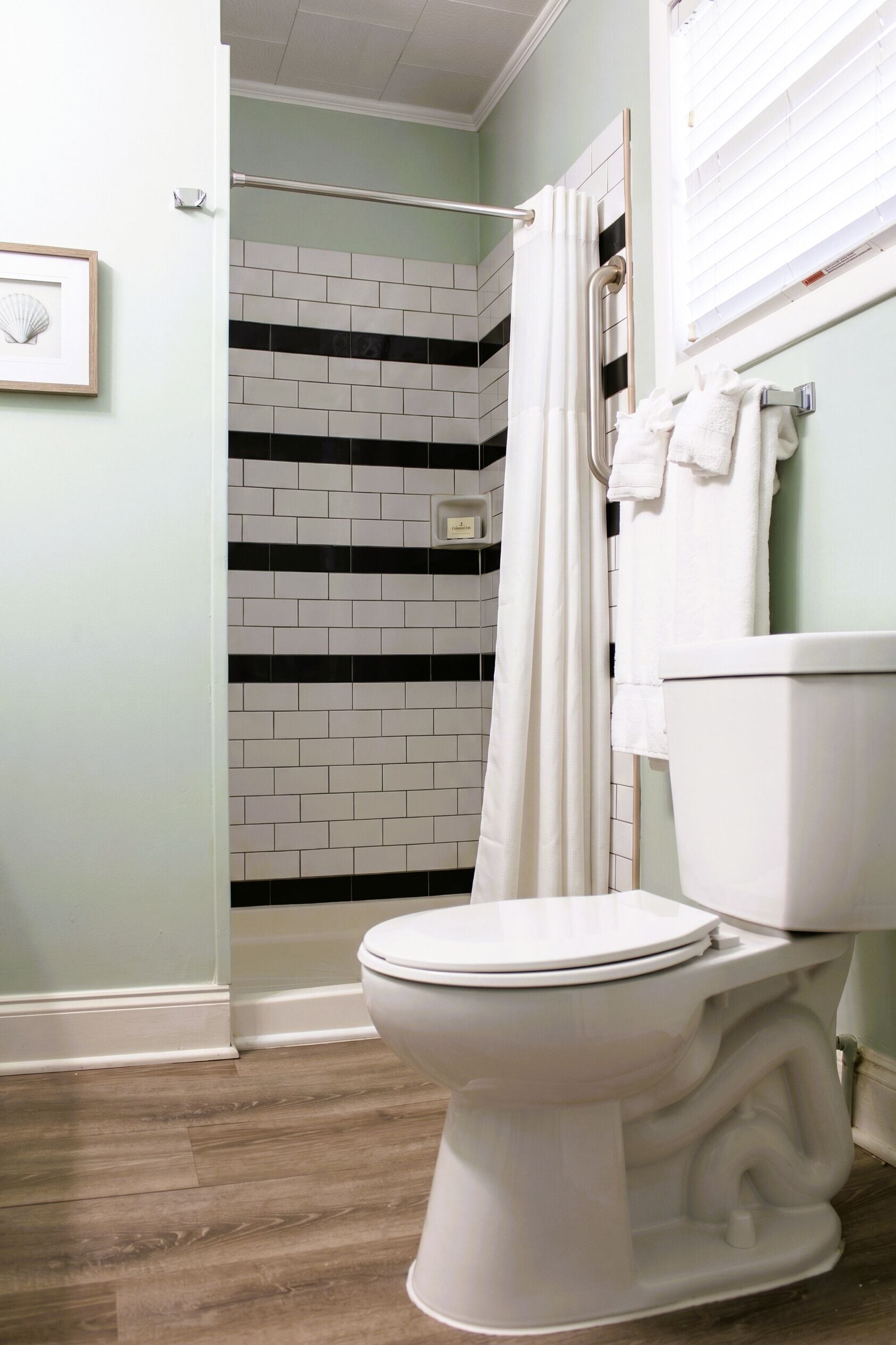 A bathroom with a white toilet, a shower with a white curtain, and a tiled wall with black and white patterns.