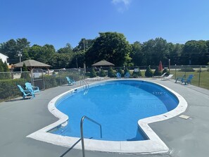 A swimming pool with a curved edge, surrounded by a fence, and blue chairs along the perimeter.