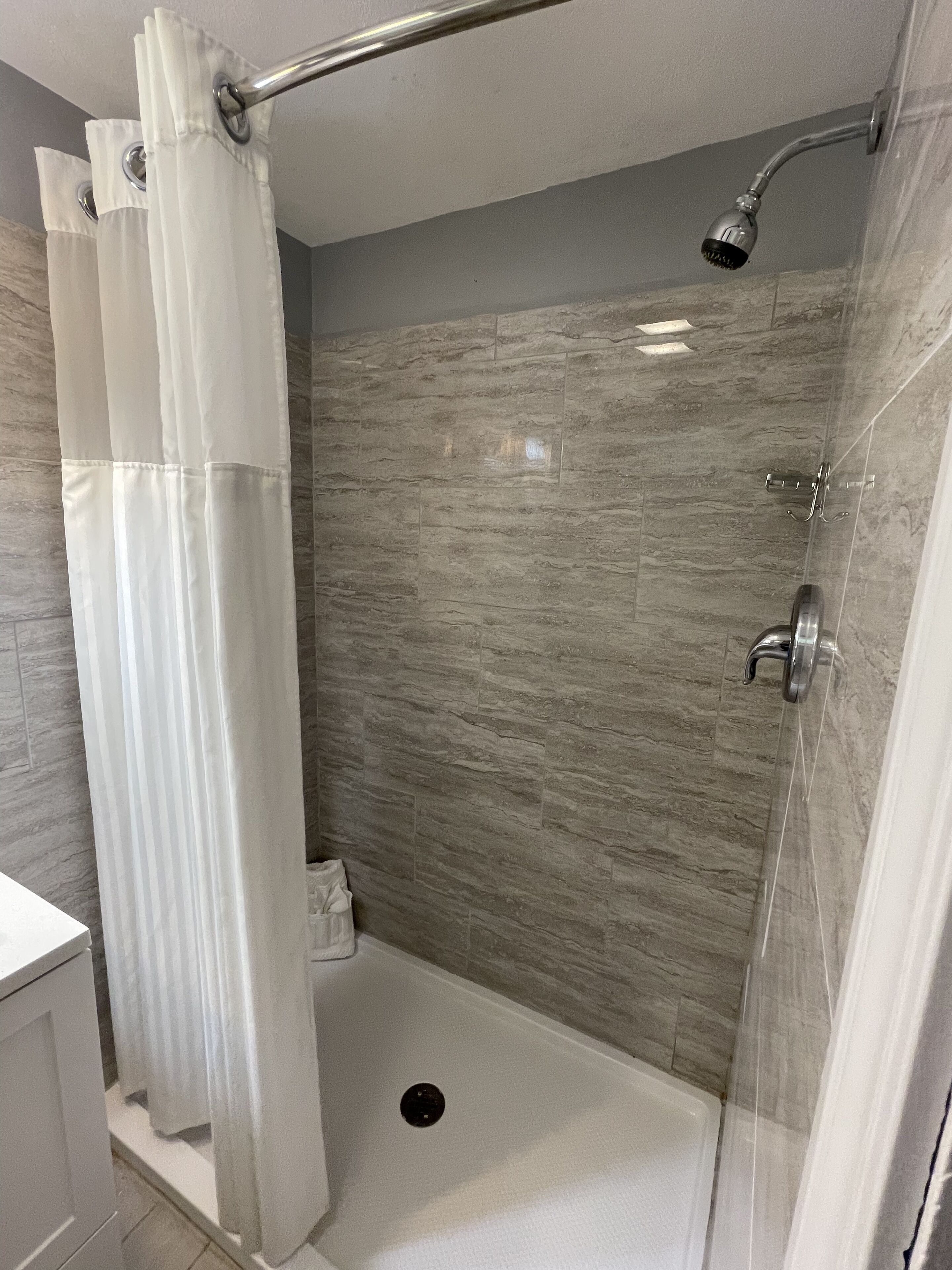 A shower with a glass door, a handheld showerhead, and a wall-mounted faucet.