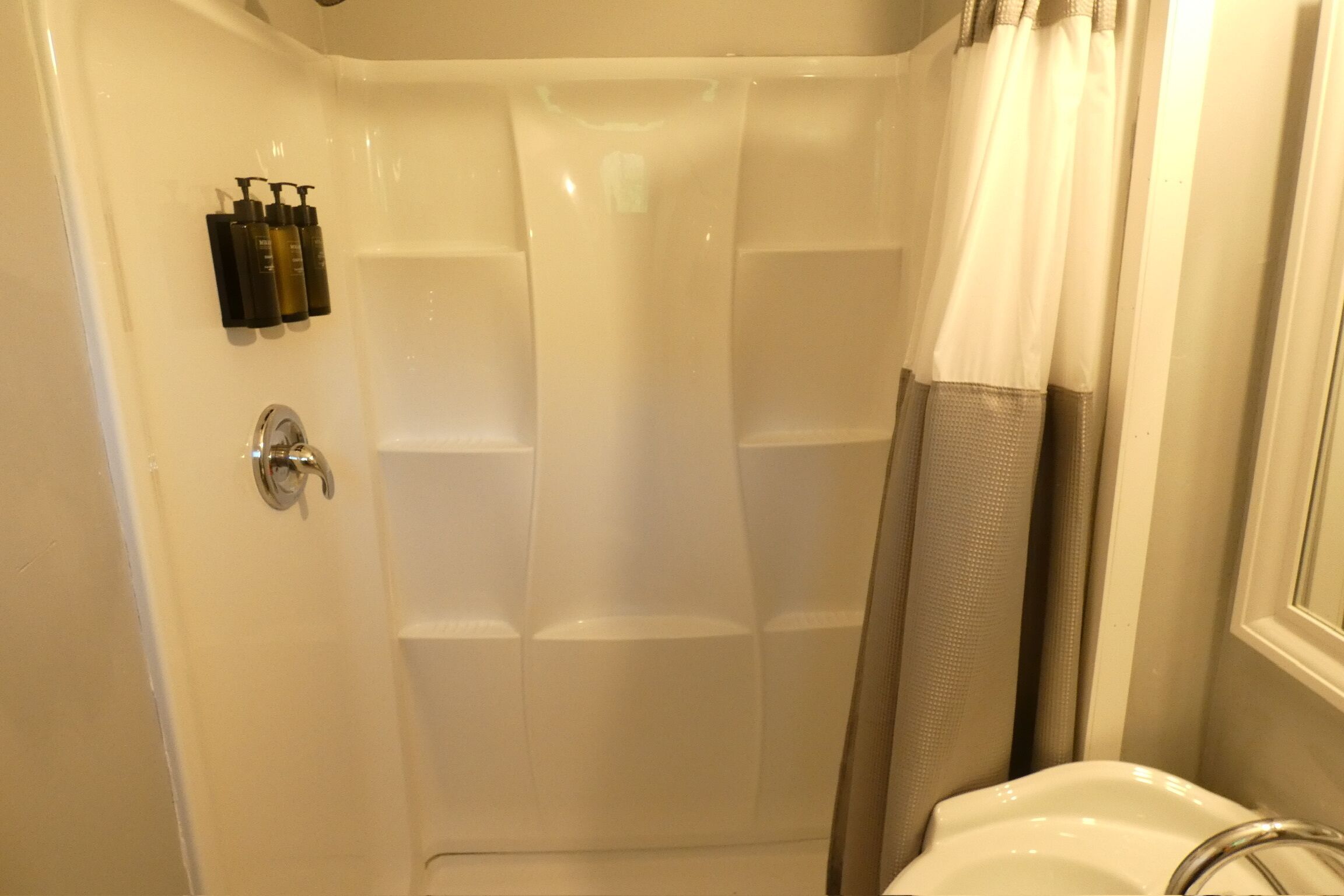 Una doccia con porta in vetro, un lavandino con rubinetto cromato e articoli da bagno a parete.