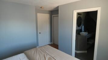 Un dormitorio con cama, una puerta y un baño visibles a través de un vano abierto.