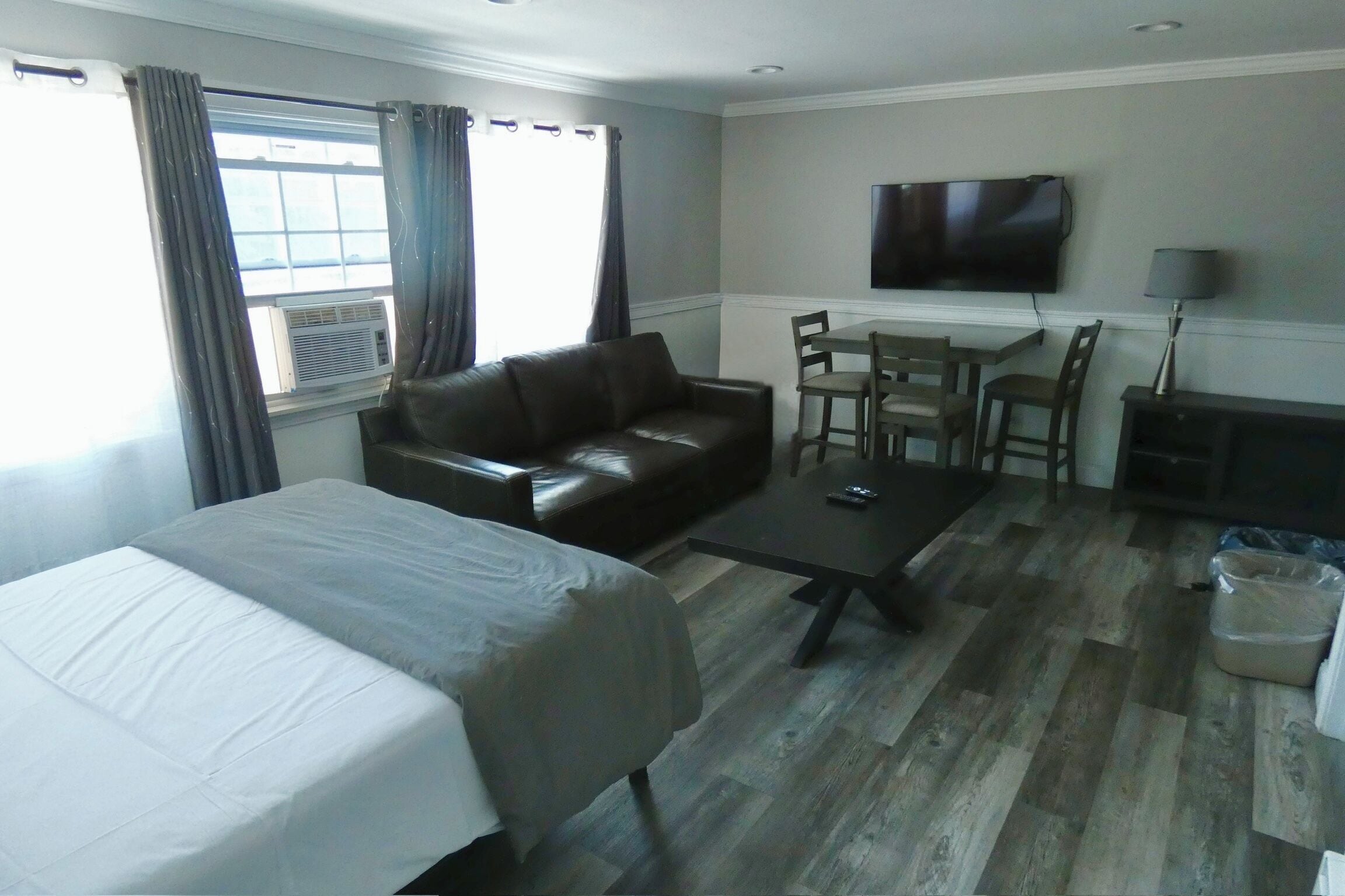 Une chambre d’hôtel comprenant un lit, un canapé en cuir, une table à manger avec des chaises, un téléviseur fixé au mur et un appareil de climatisation.