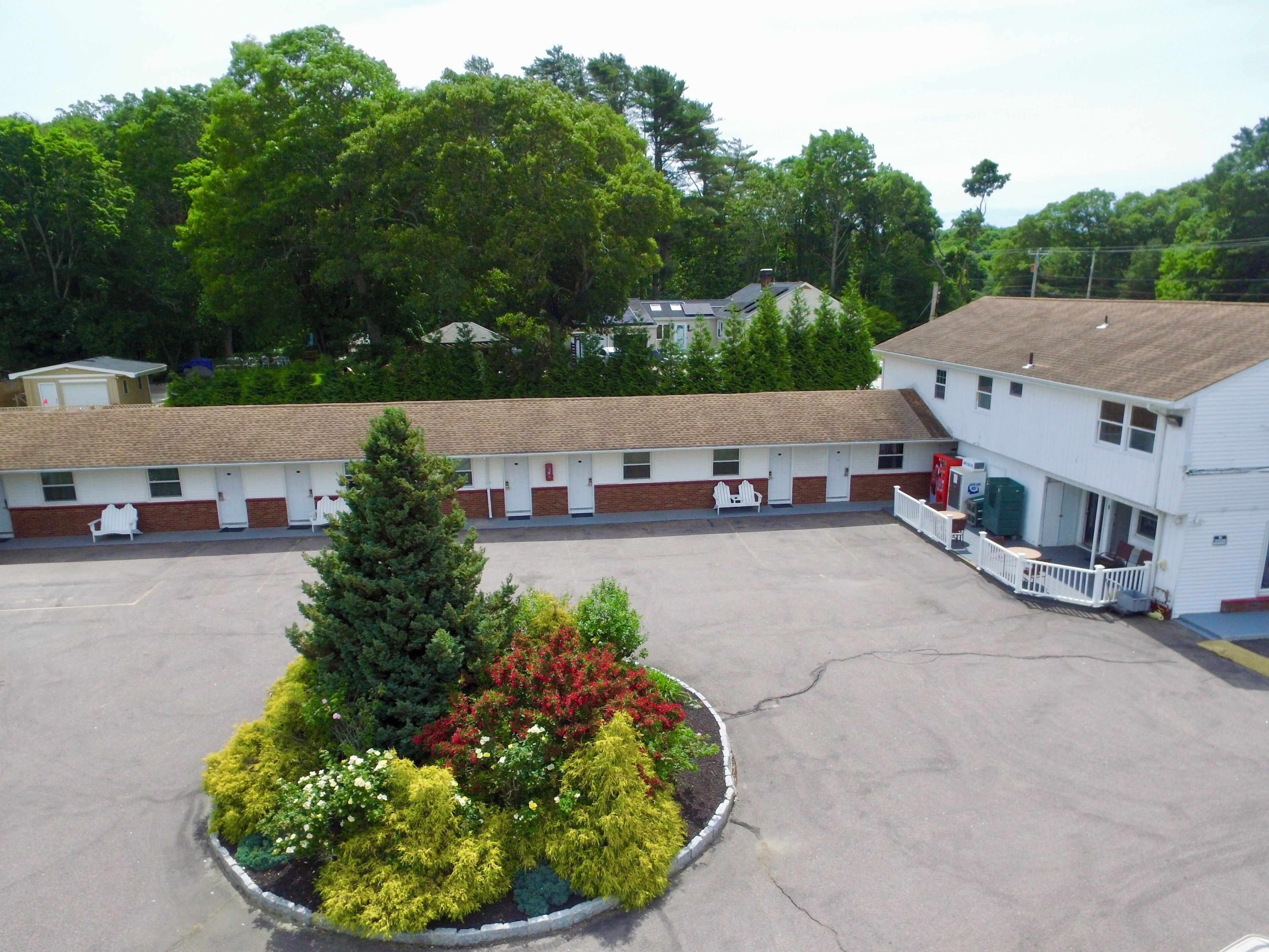 Un motel con estacionamiento, un pequeño jardín con diversas plantas y un edificio con porche.