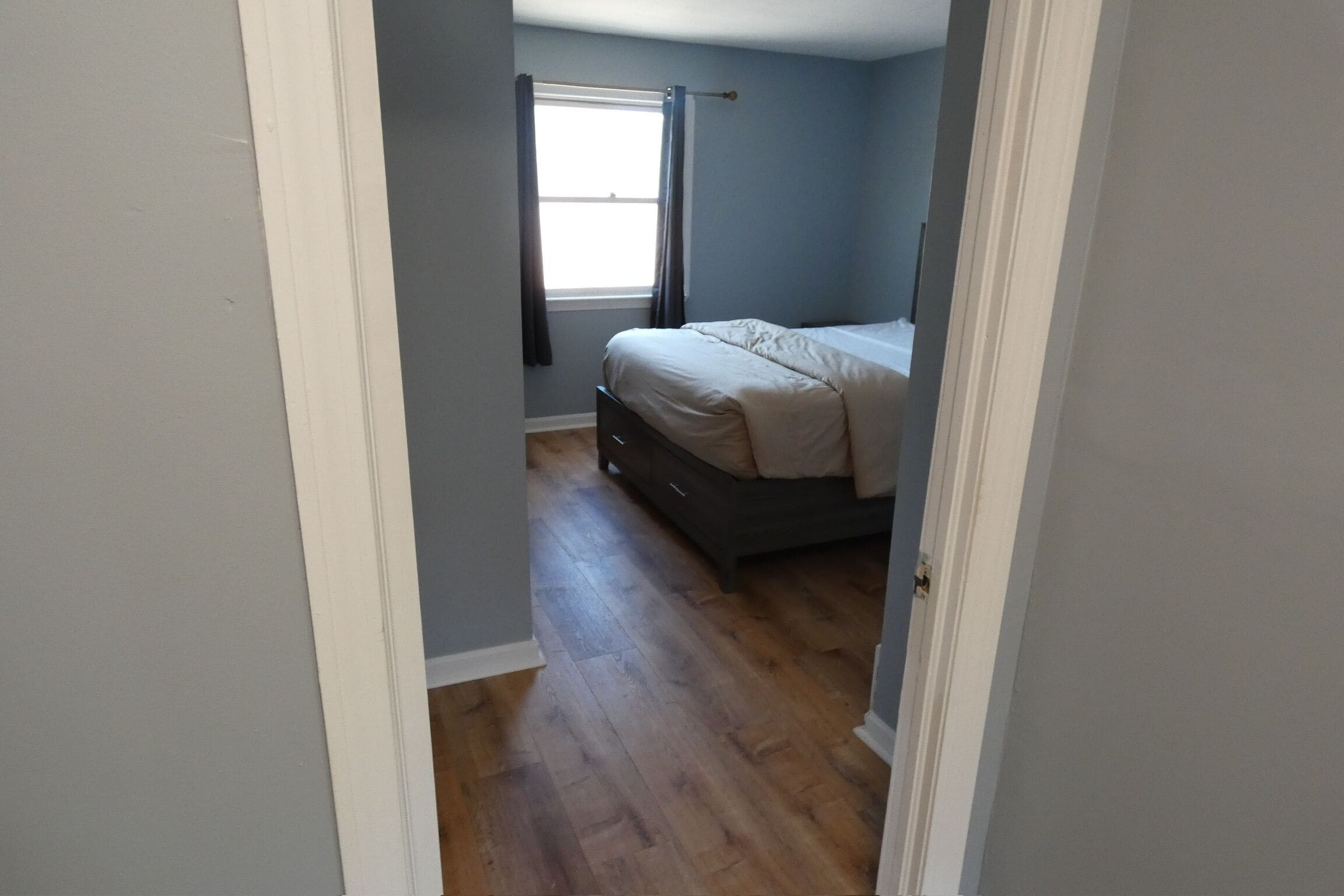 A bedroom with a bed, a window with curtains, and a wooden floor.