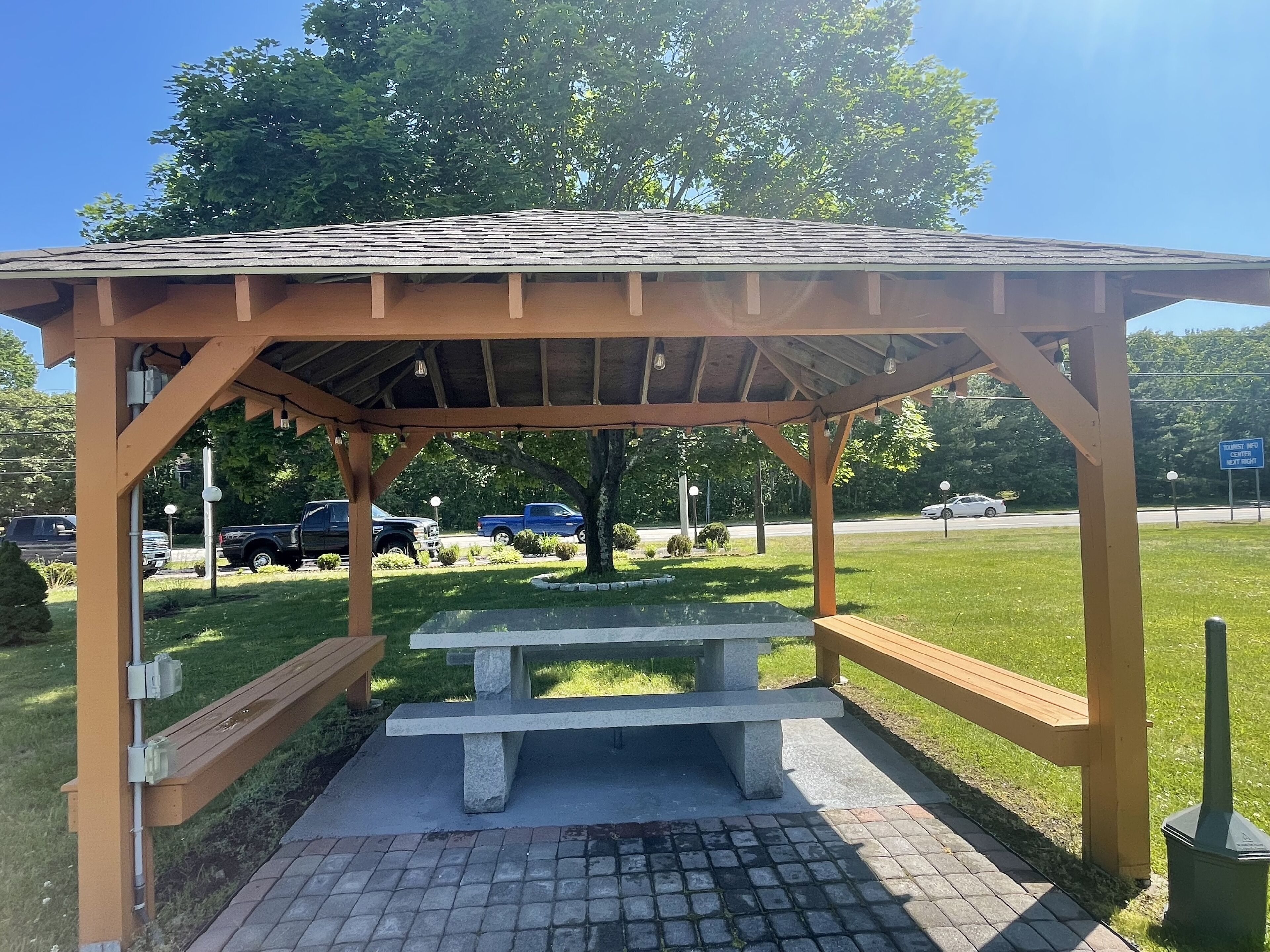 Un área de picnic techada con banco y mesa, rodeada de césped y árboles.
