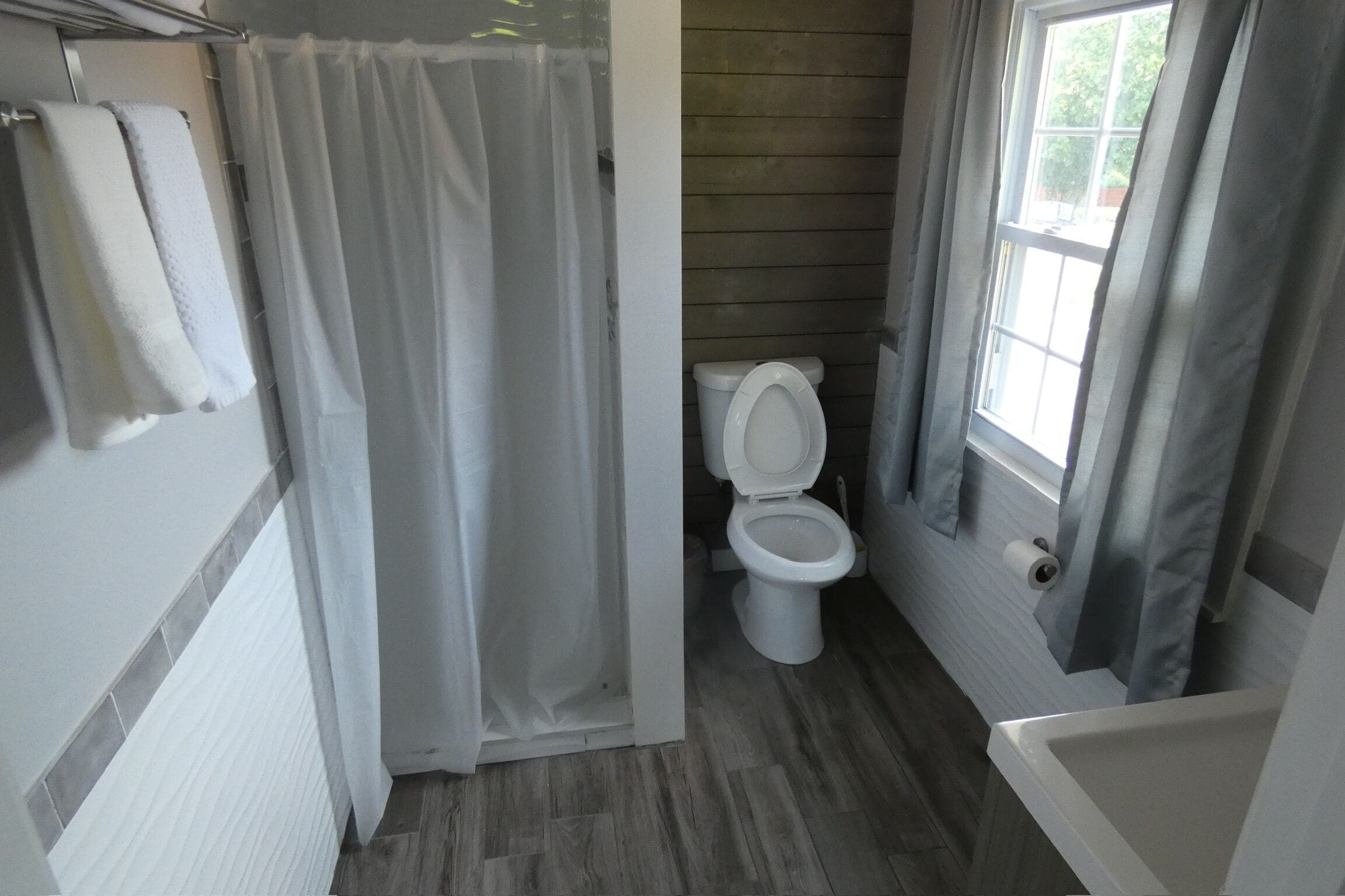 Een badkamer met douchegordijn, toilet, raam en handdoekhouder.