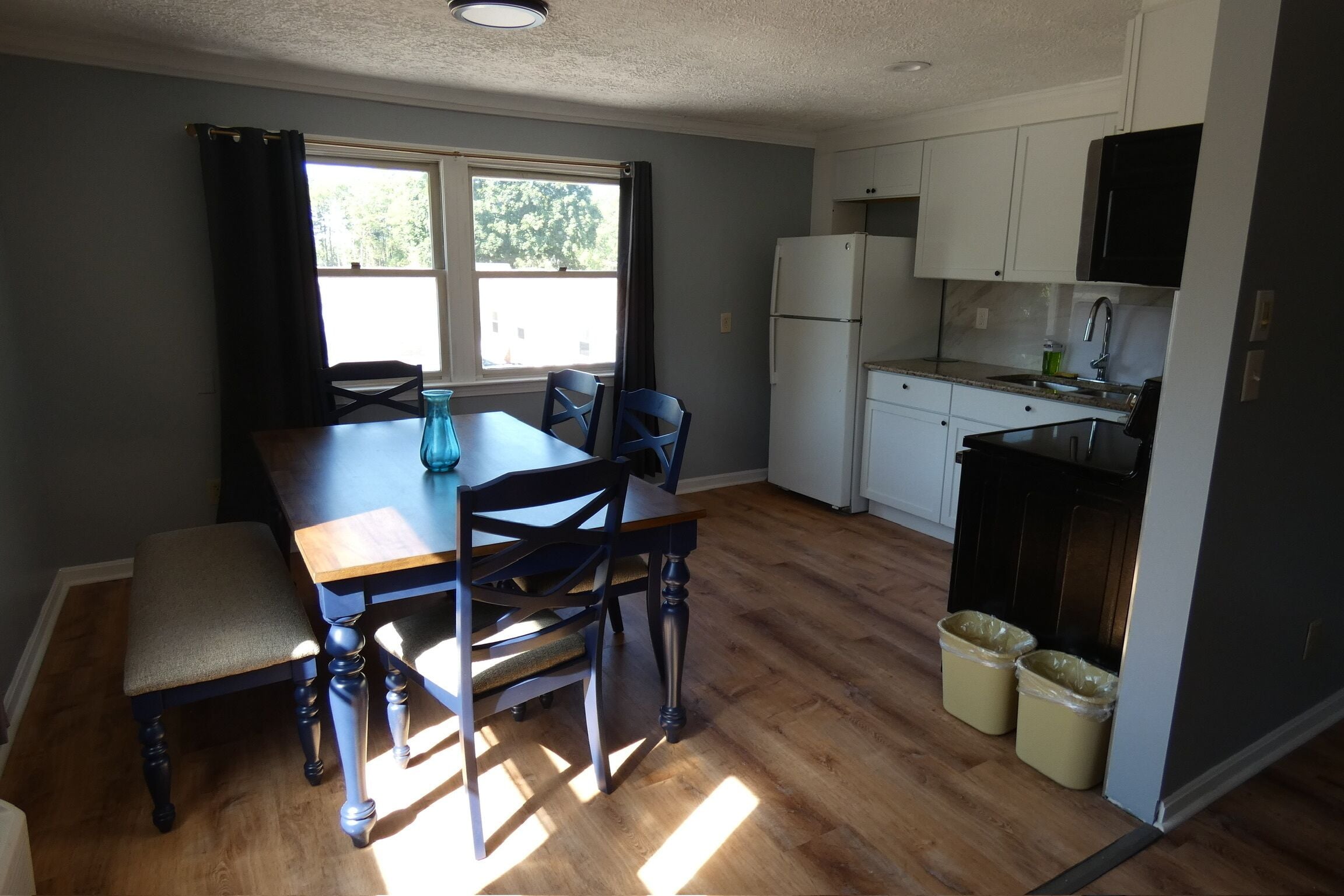 Une cuisine compacte comprenant une table à manger, des chaises, un réfrigérateur et deux poubelles.