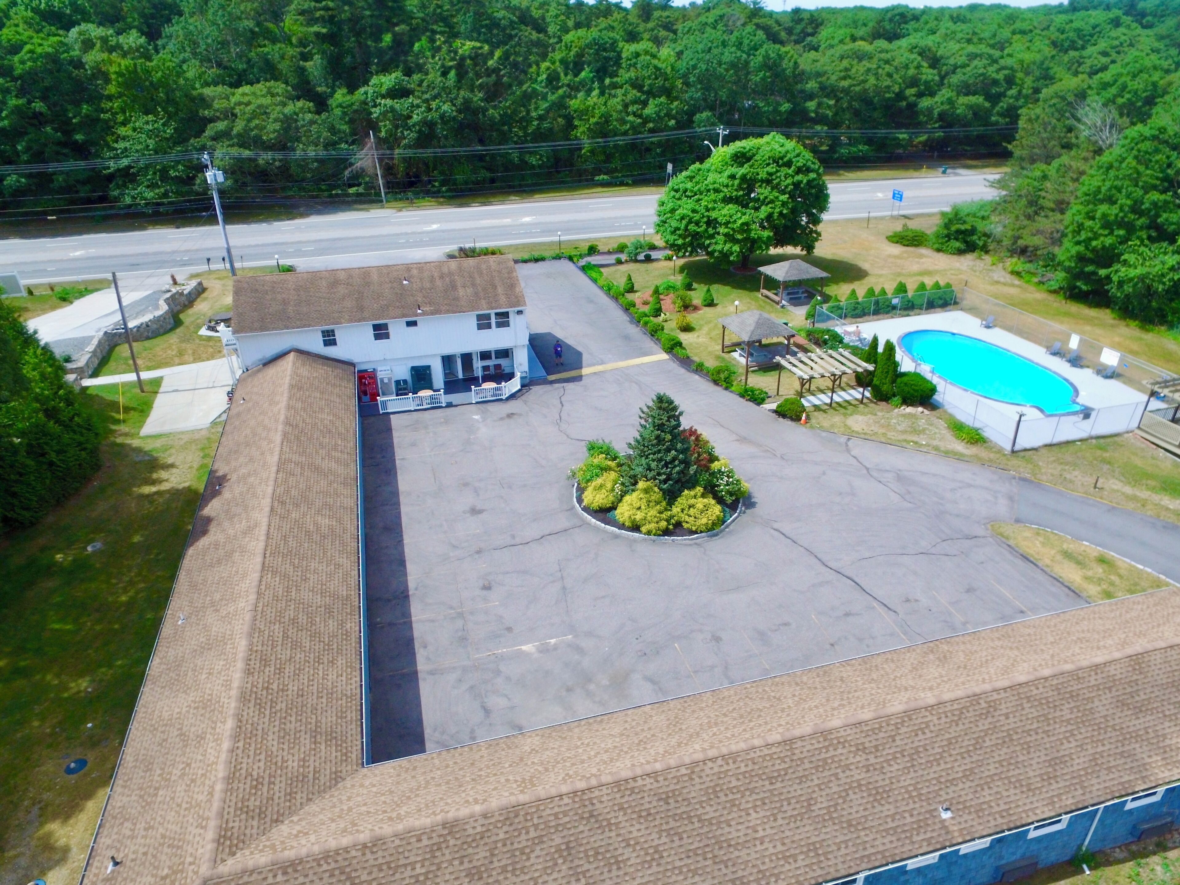 An aerial view of a building with a swimming pool, a covered pavilion, and a landscaped area with a tree and shrubs.