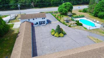 An aerial view of a building with a swimming pool, a covered pavilion, and a landscaped area with a tree and shrubs.