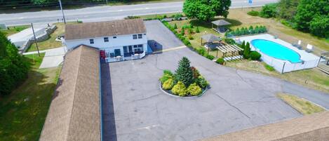 An aerial view of a building with a swimming pool, a covered pavilion, and a landscaped area with a tree and shrubs.