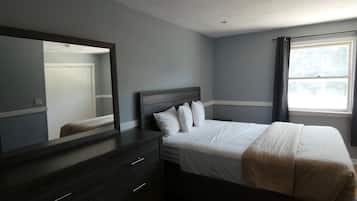 A bedroom with a bed, a dresser, a mirror, and a window.