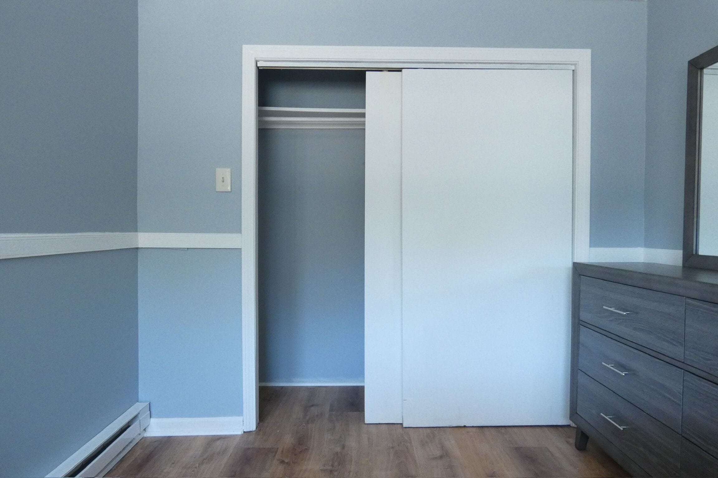 Ein Zimmer mit geschlossener Tür, einem Schminktisch und einem Lichtschalter an der Wand.