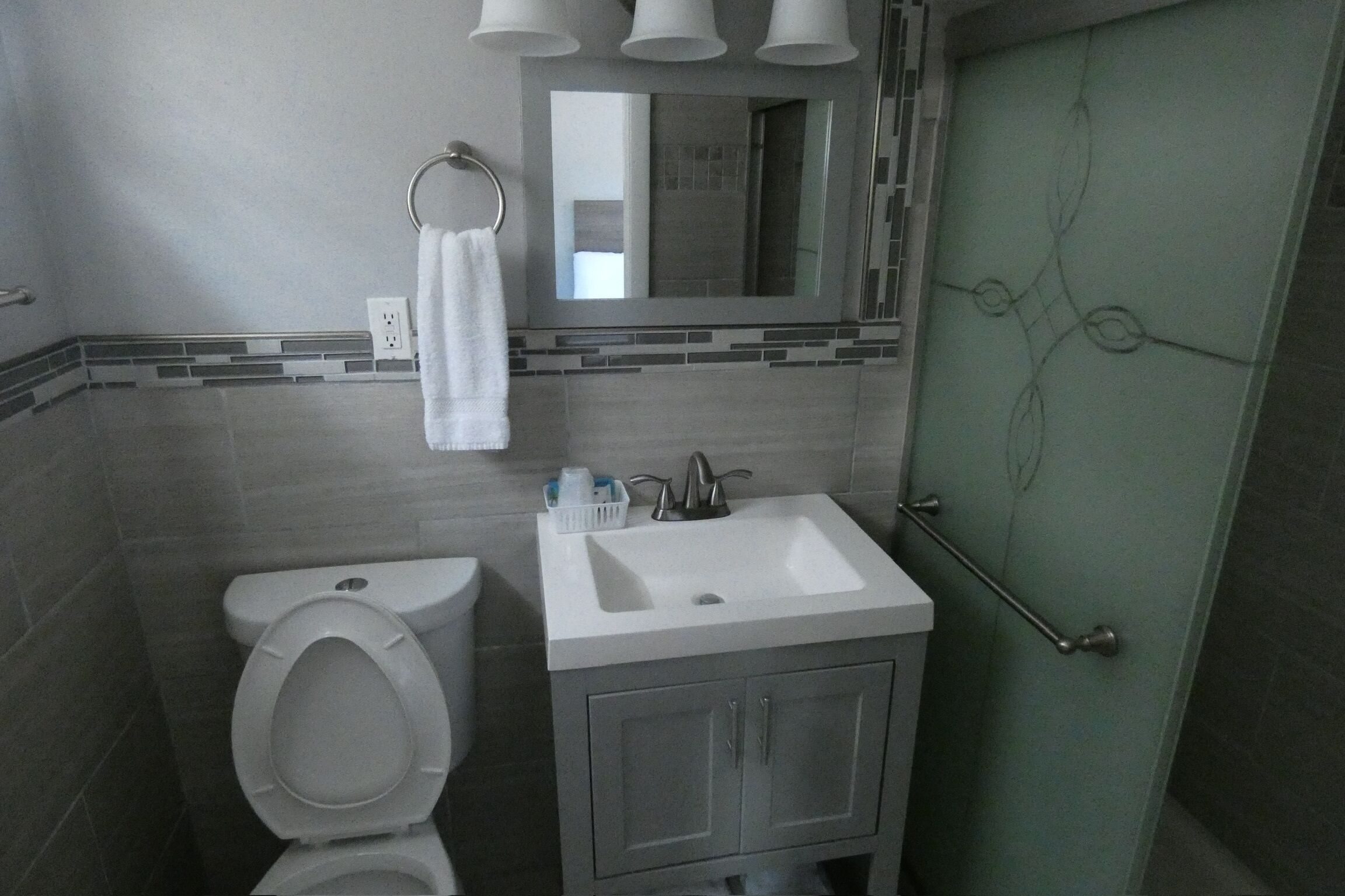 Un baño con inodoro, lavamanos, espejo y perchero para toallas.