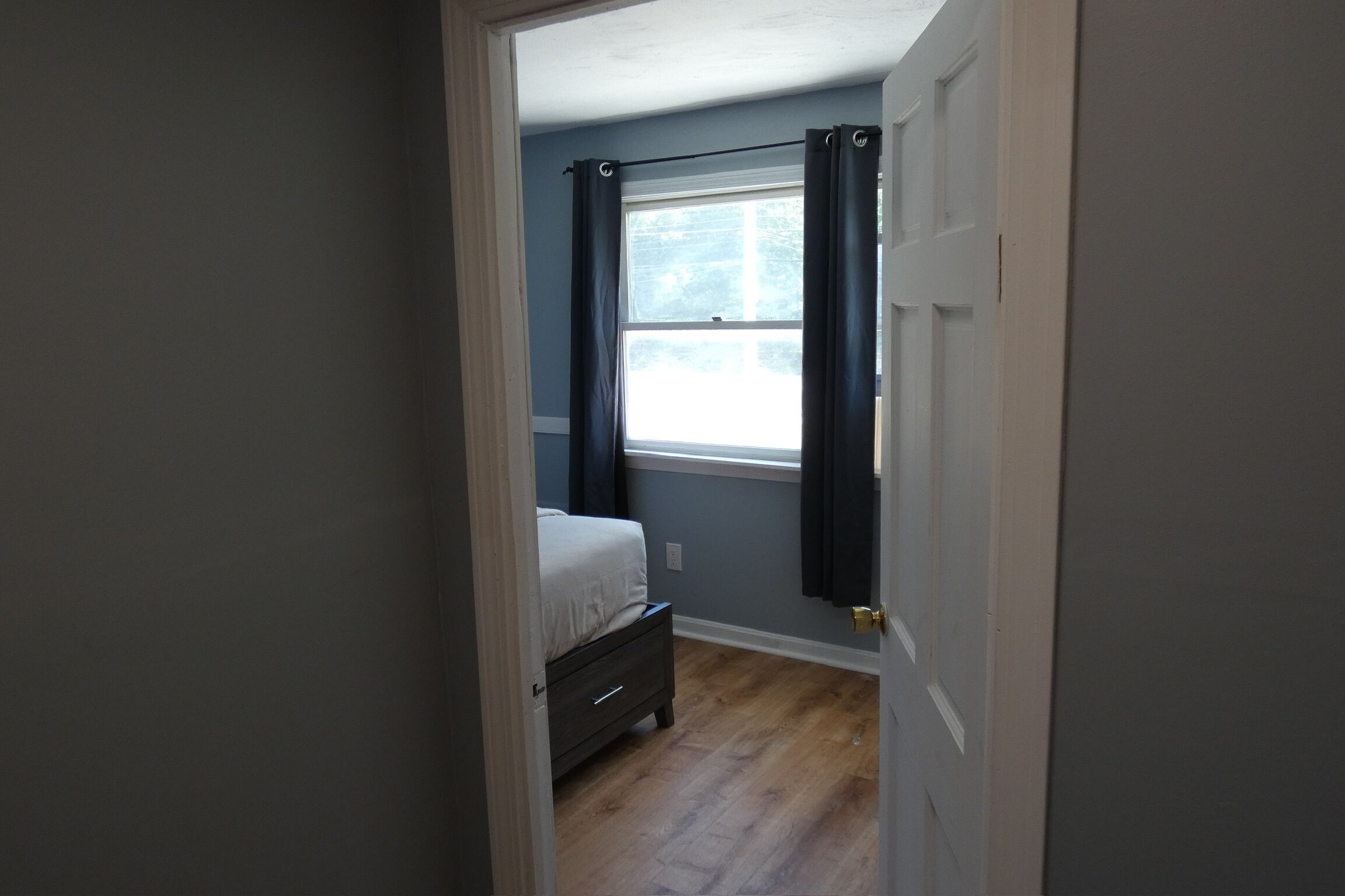 Ein Schlafzimmer mit einem Bett, einem Fenster mit Vorhängen und einer Tür.