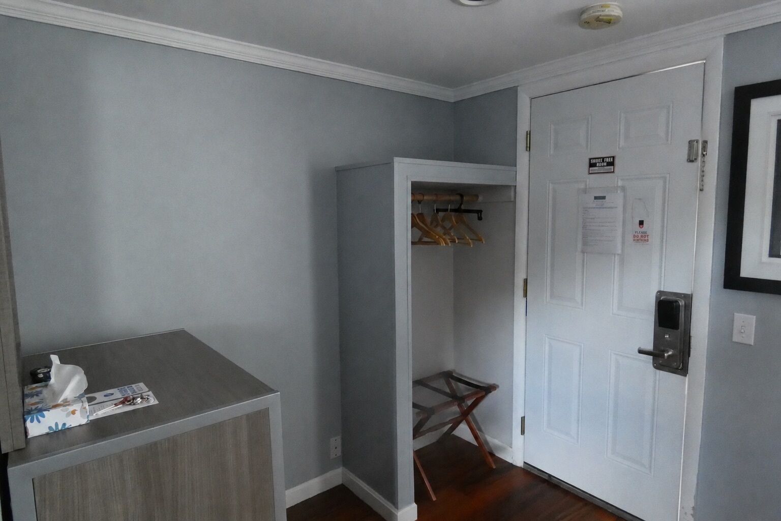 A room with a grey wall, a white door, a coat rack, and a small wooden chair.