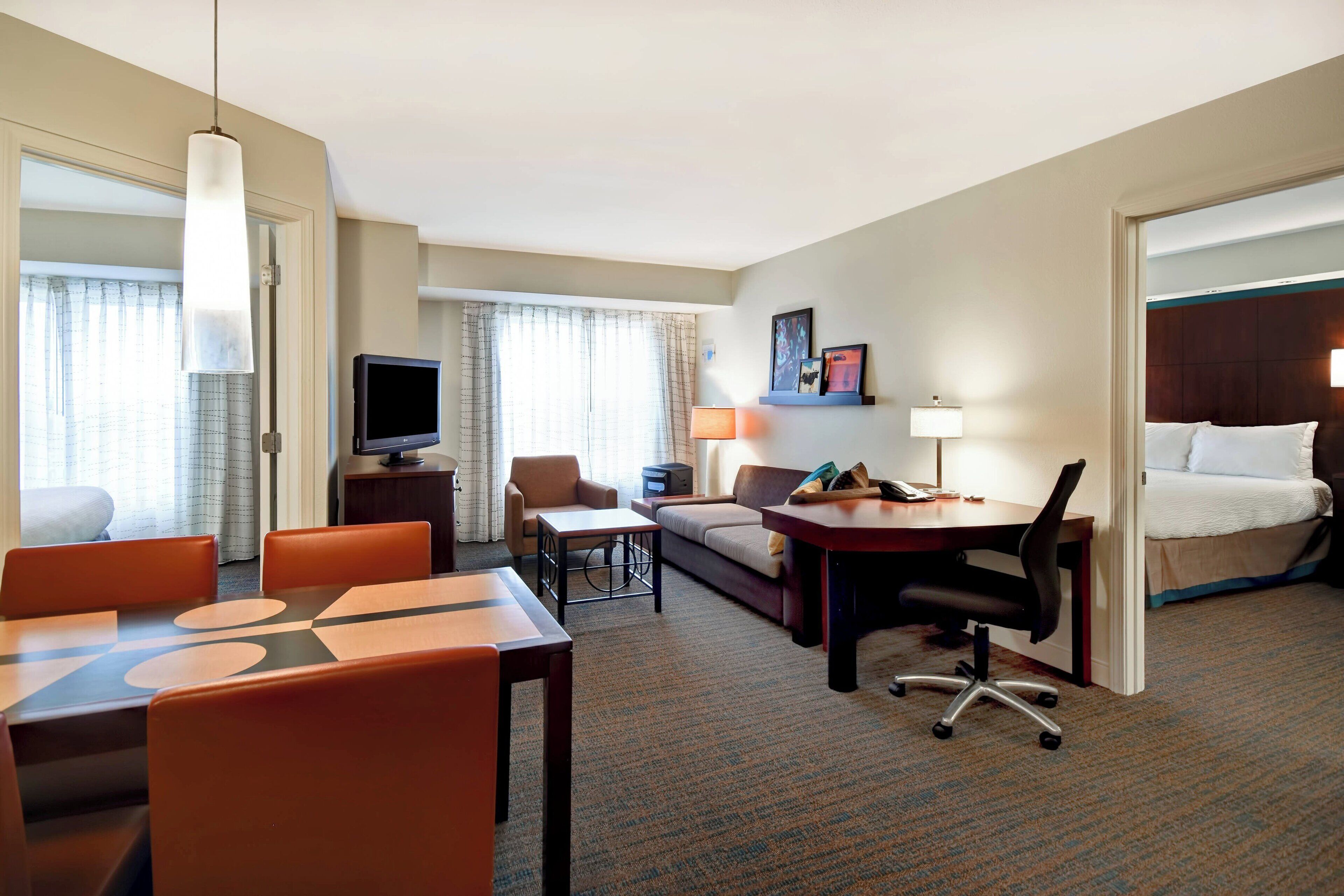 Habitación de hotel con zona de comedor, sofá, escritorio, televisión y cama.