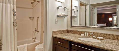 A bathroom with a bathtub, toilet, vanity with a sink, and a large mirror.