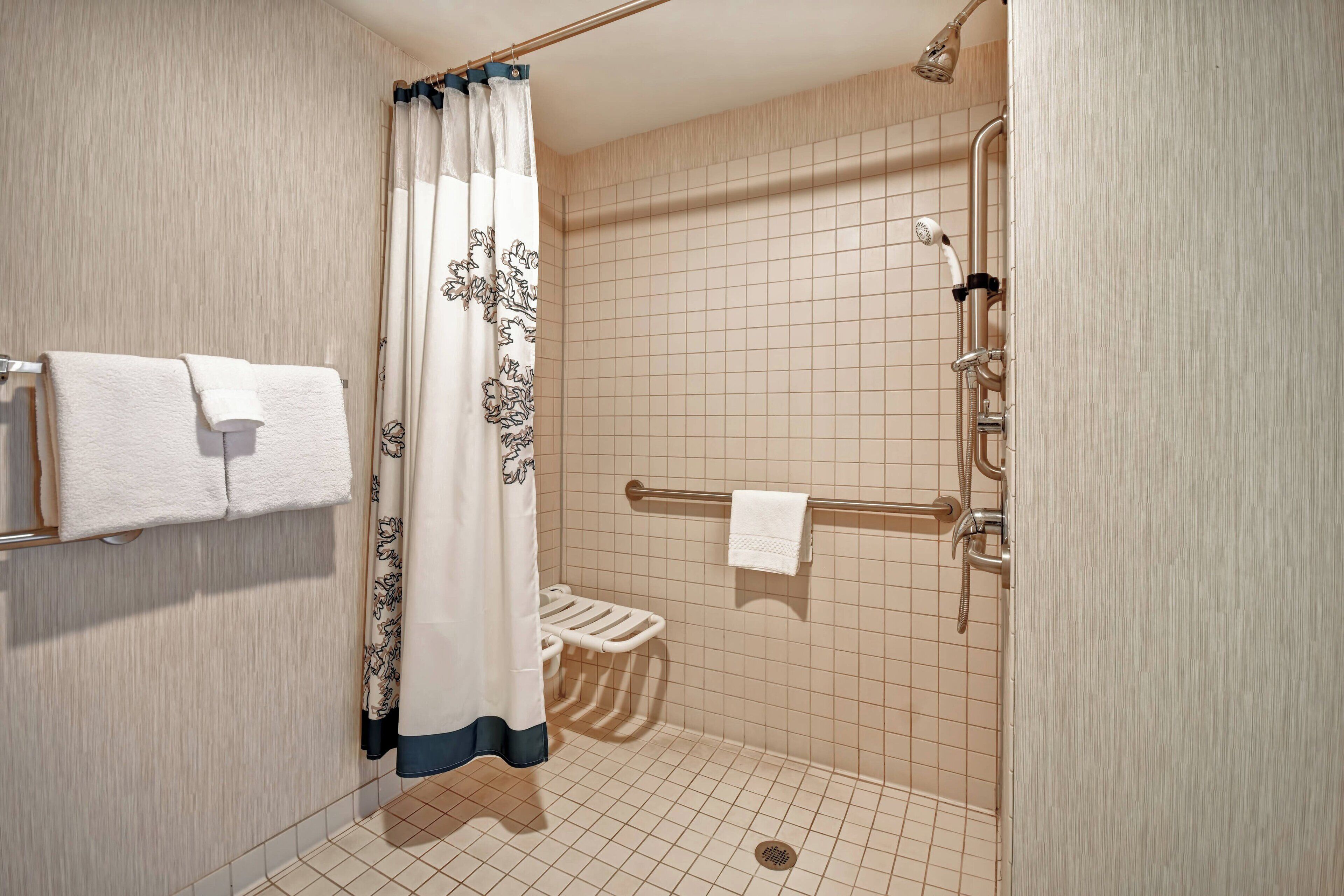 A shower with a handheld showerhead, a towel rack, and a toilet with a grab bar.