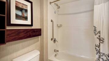 A bathroom with a white toilet, a framed picture on the wall, a bathtub with a shower curtain, and a handrail.