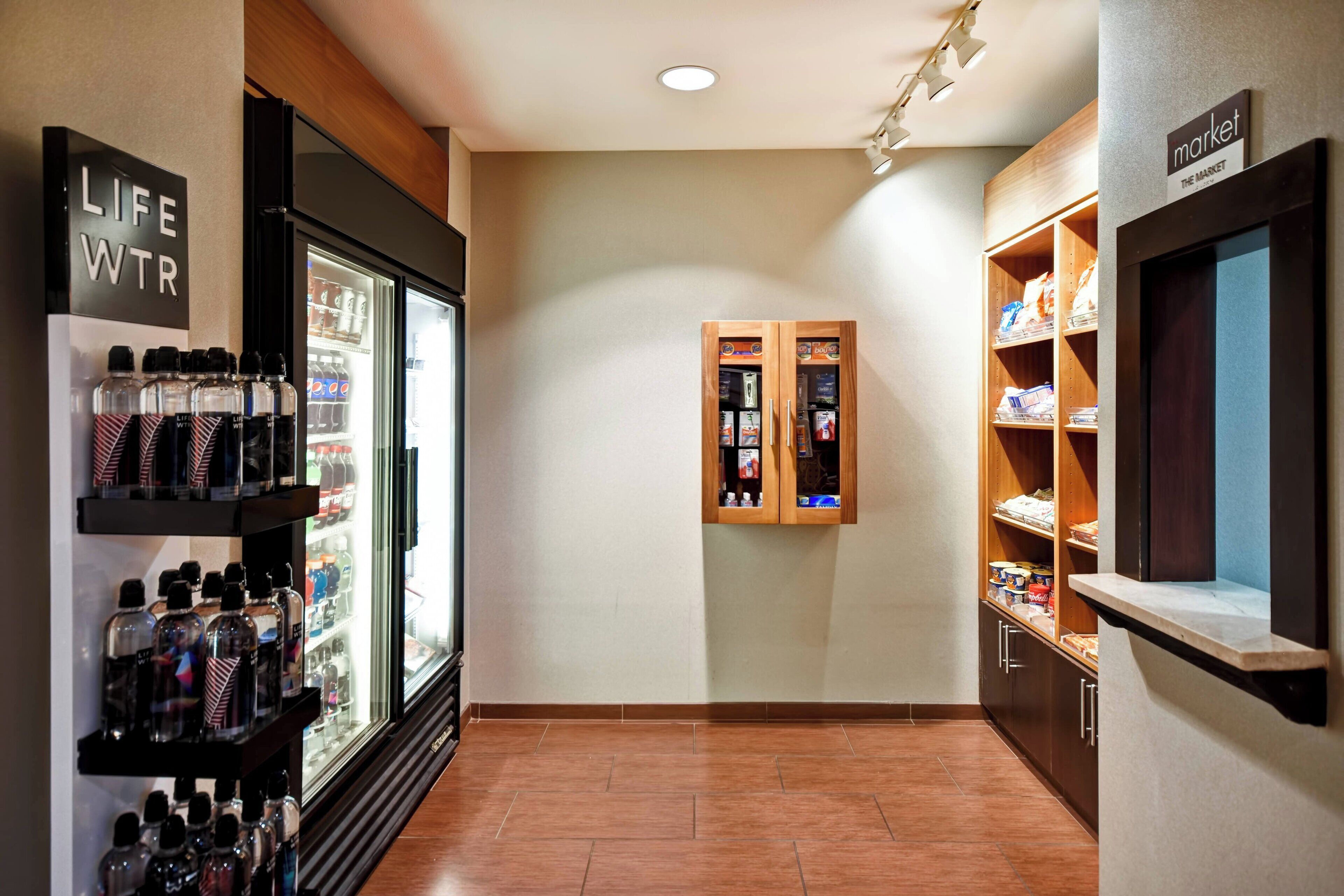 A hallway with a refrigerated display, a life water station, and a market area with shelves.