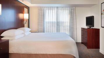A hotel room with a large bed, a wooden dresser, a television, and a window with curtains.
