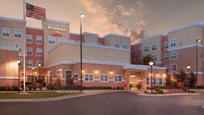 A multi-story hotel with a prominent American flag, a well-lit entrance, and a landscaped courtyard. - Residence Inn by Marriott Stillwater (Stillwater)