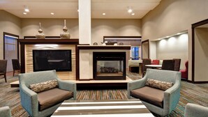A hotel lobby with a fireplace, two armchairs with cushions, a striped rug, and a television. - Residence Inn by Marriott Stillwater (Stillwater)