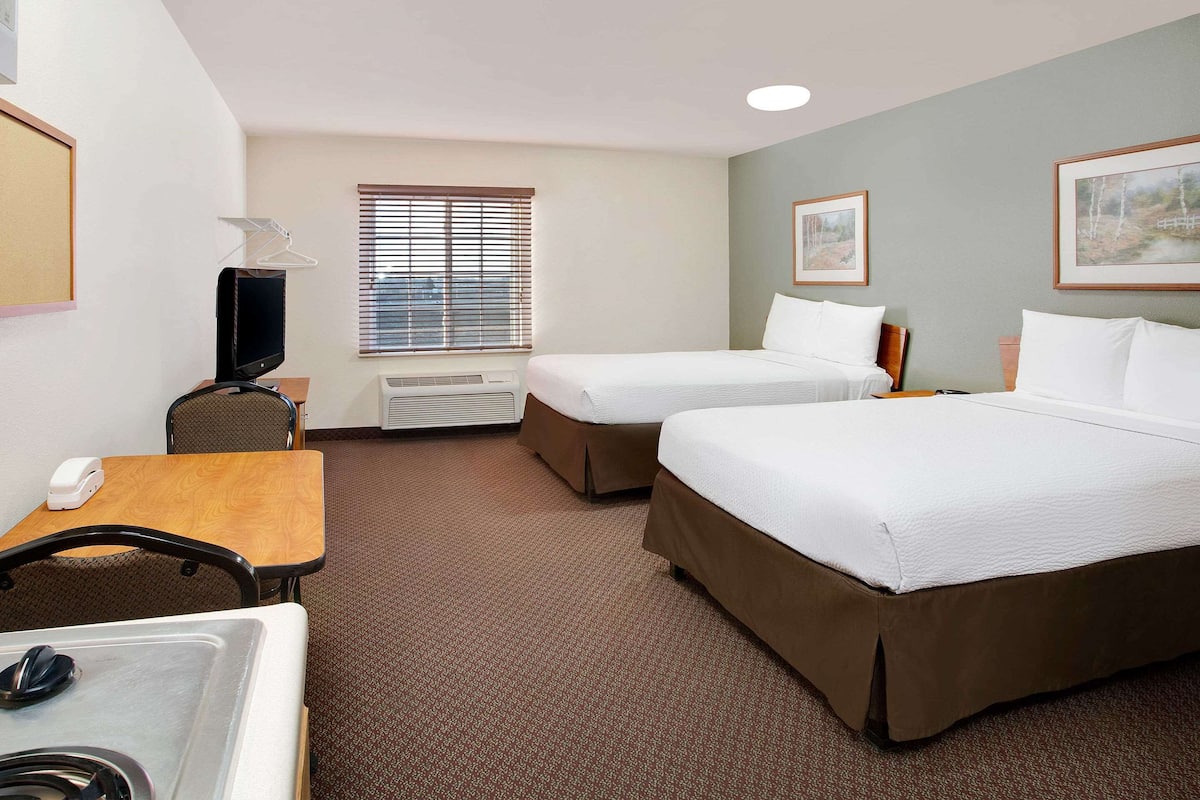 A hotel room with two beds, a desk, a chair, a TV, and a window with blinds.