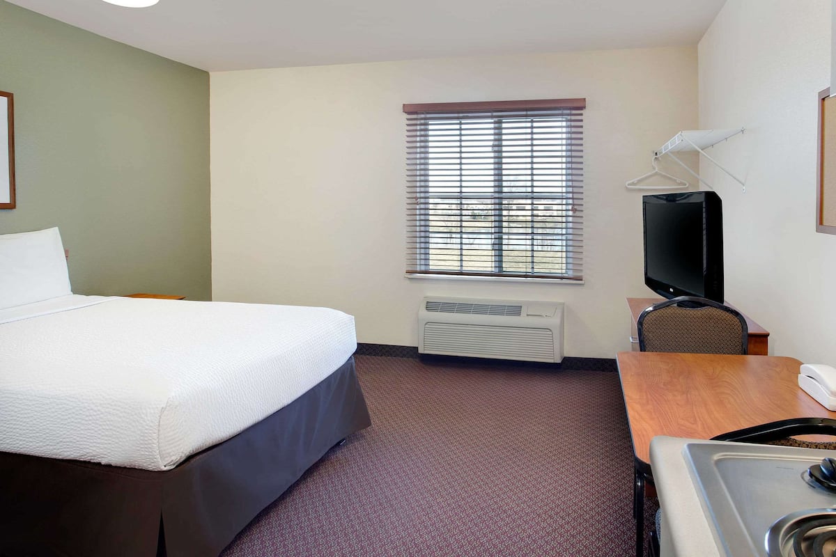 A hotel room with a bed, a desk, a chair, a television, and a window with blinds.