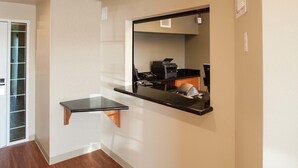 A hallway with a wooden floor, a small black desk with a mirror, and a door with a glass panel. - WoodSpring Suites Fort Wayne (Fort Wayne)