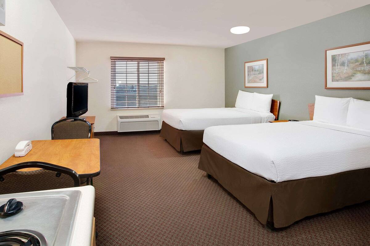 A hotel room with two beds, a desk, a chair, a TV, and a window with blinds.