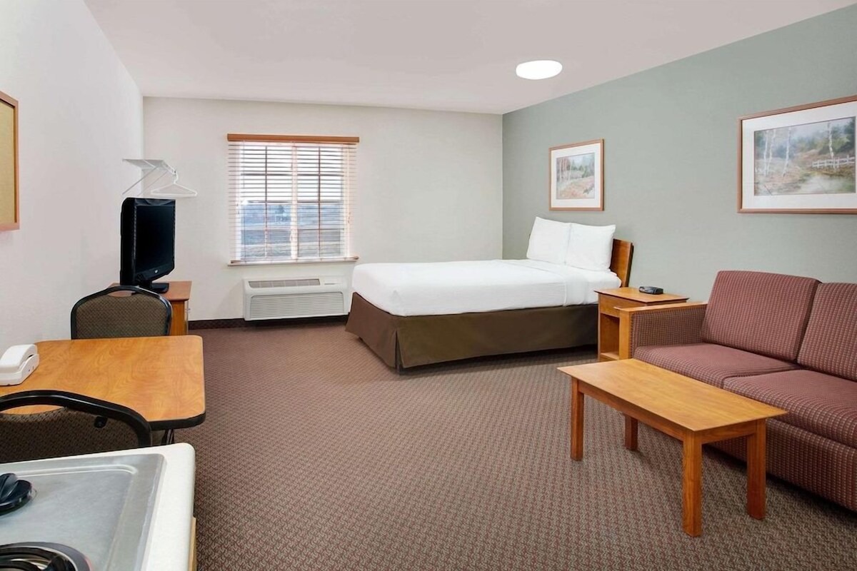 A hotel room with a bed, a sofa, a desk, a chair, a television, and a window with blinds.