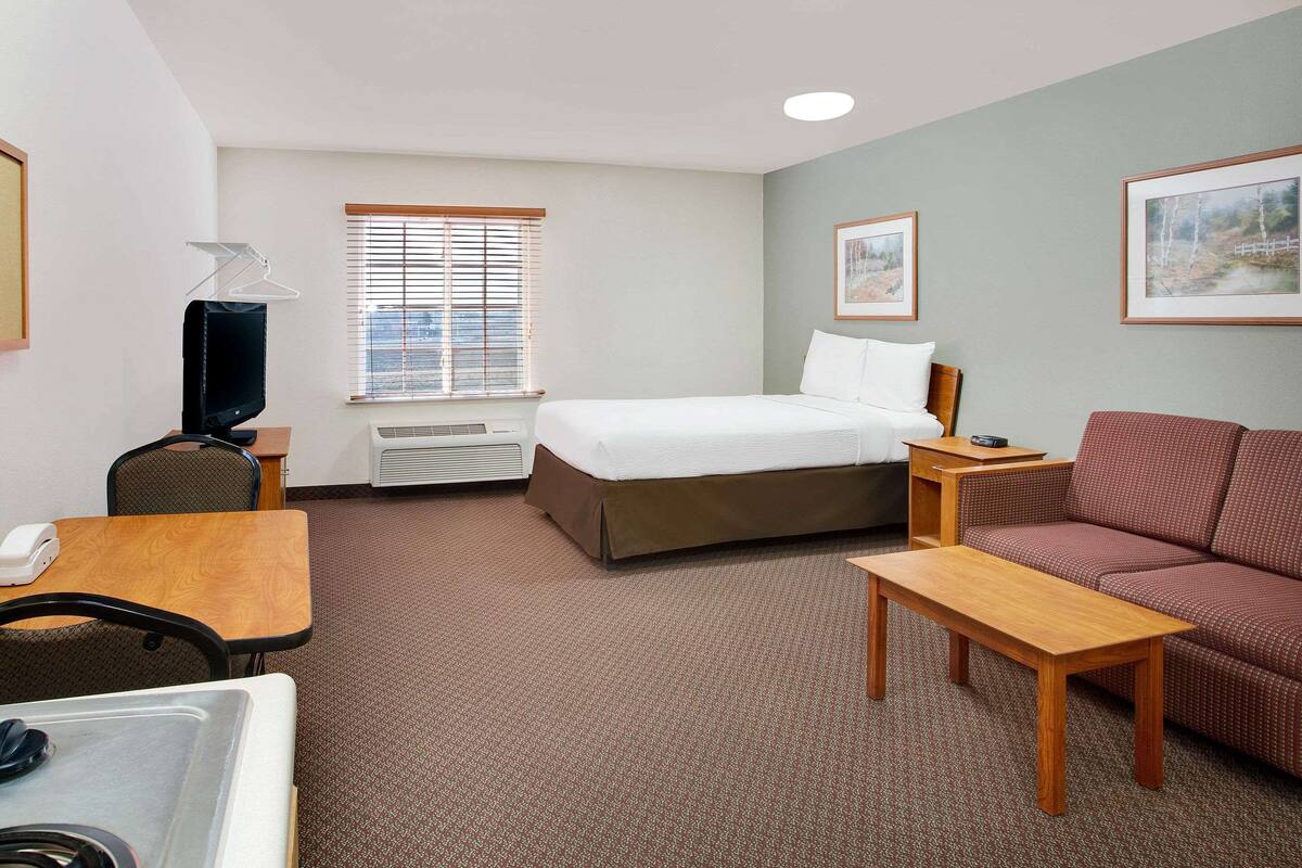 A hotel room with a bed, a sofa, a desk, a chair, a television, and a window with blinds.