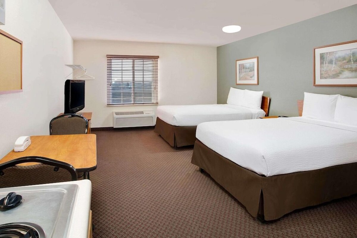 A hotel room with two beds, a desk with a telephone, a TV, and a window with blinds.