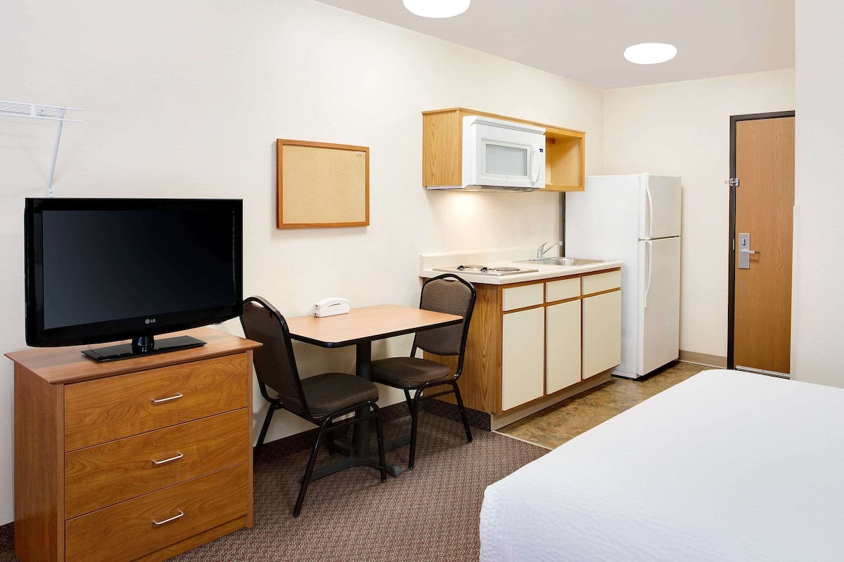 A hotel room with a bed, a desk with a chair, a television, a microwave, a refrigerator, and a wooden cabinet.