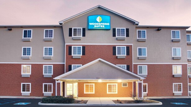 A multi-story hotel with a prominent "Woodspring Suites" sign. It features a brick facade with multiple windows and a central entrance. - WoodSpring Suites Fort Wayne (Fort Wayne)