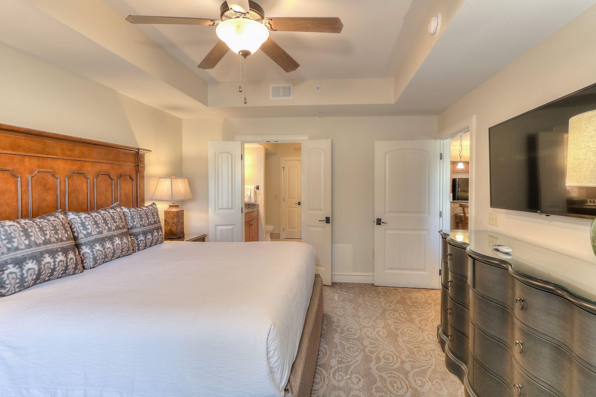 A bedroom with a bed, a ceiling fan, a dresser, and a television.