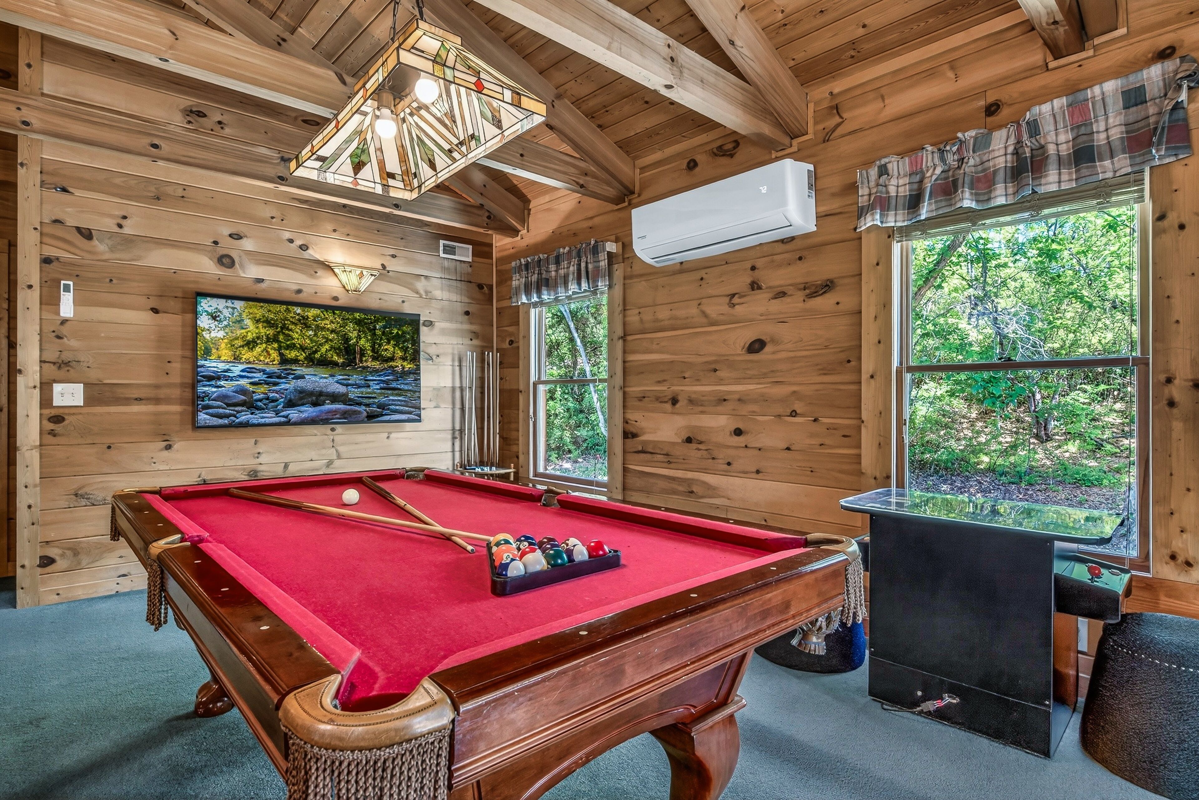 A wooden interior with a pool table, a television, and a fireplace.