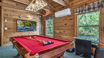 A wooden interior with a pool table, a television, and a fireplace.