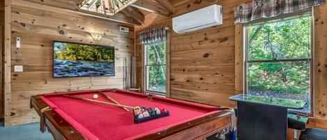 Un interior de madera con mesa de billar, televisor y chimenea.
