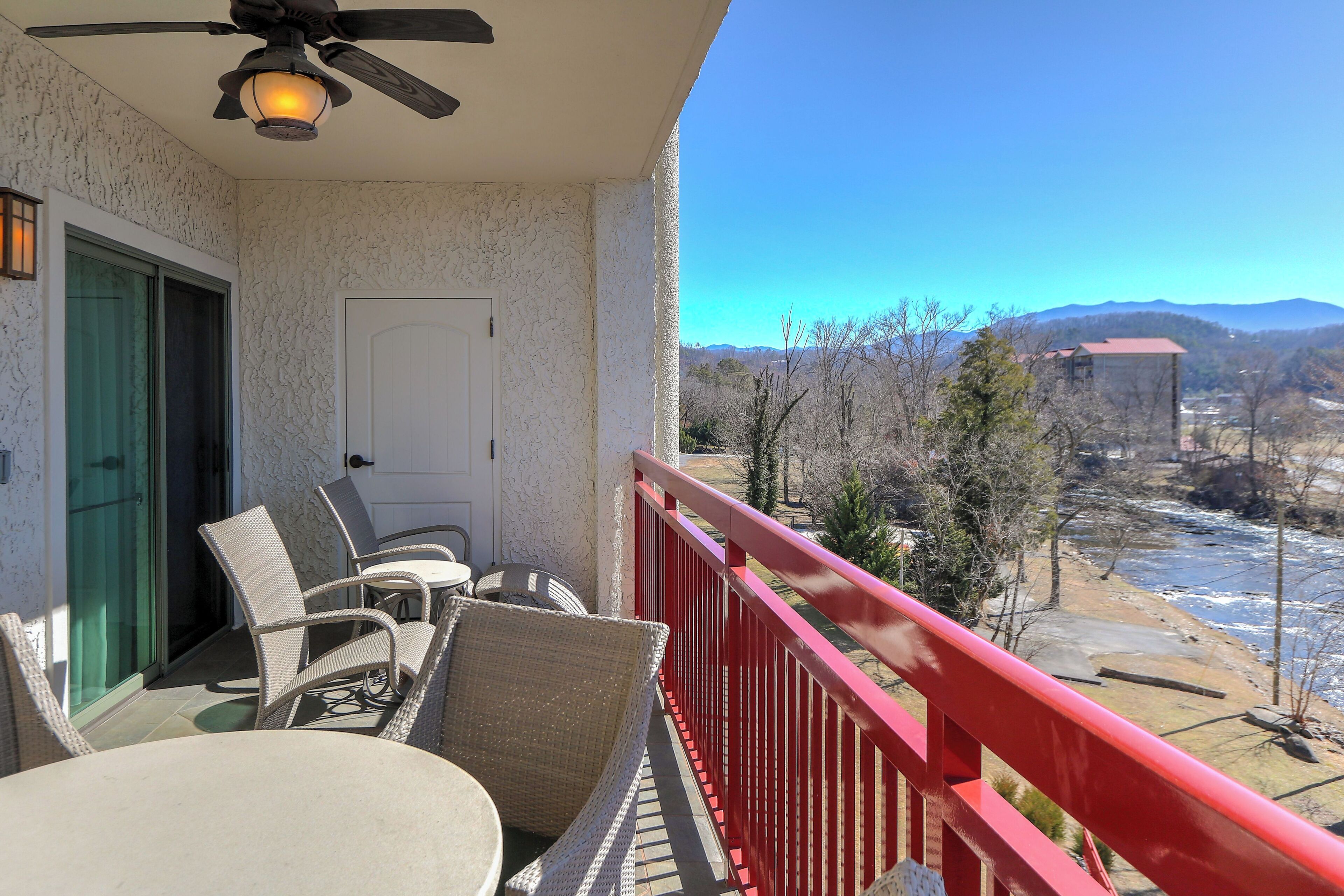 A balcony with wicker furniture, a ceiling fan, and a view of a river and mountains.