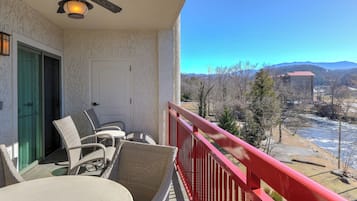 A balcony with wicker furniture, a ceiling fan, and a view of a river and mountains.