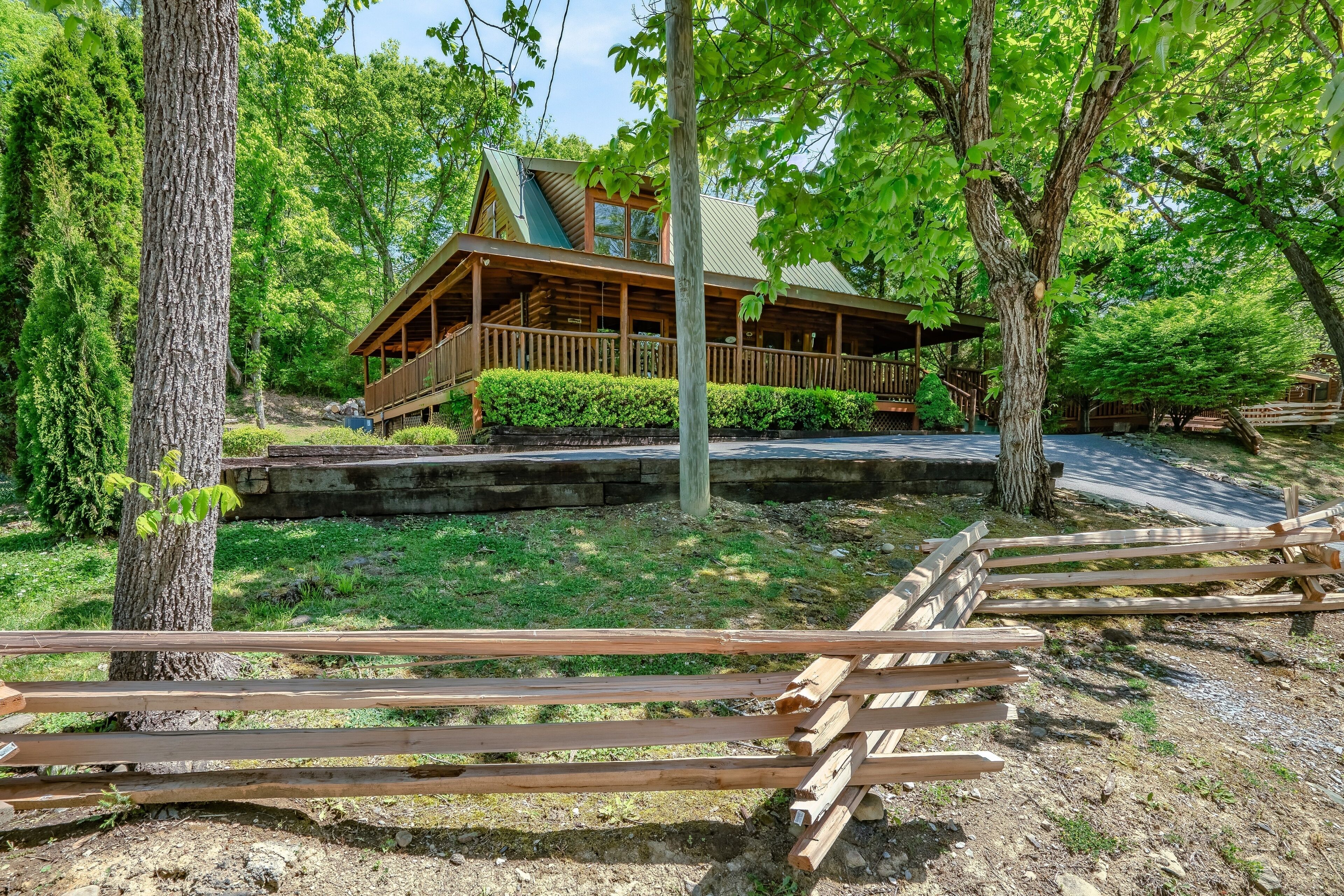 A cabin with a porch, surrounded by trees and a wooden fence.