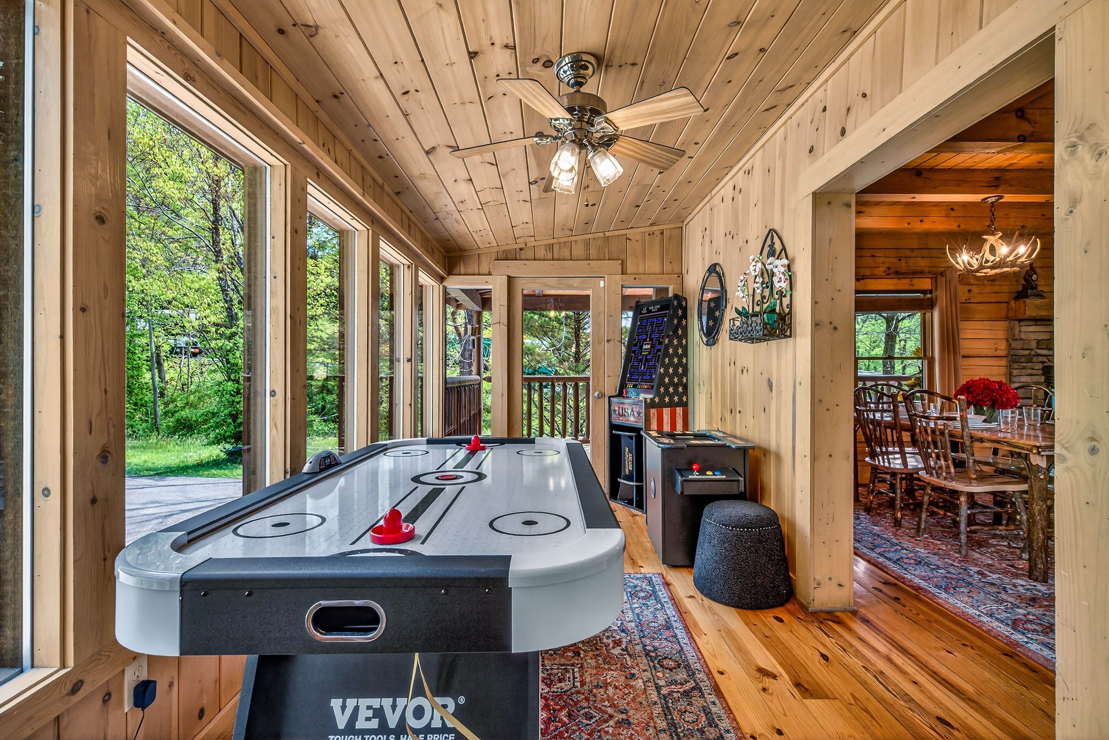 A wooden interior with a pool table, a ceiling fan, and a dining area with a rug.