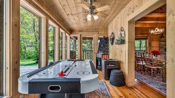 A wooden interior with a pool table, a ceiling fan, and a dining area with a rug.