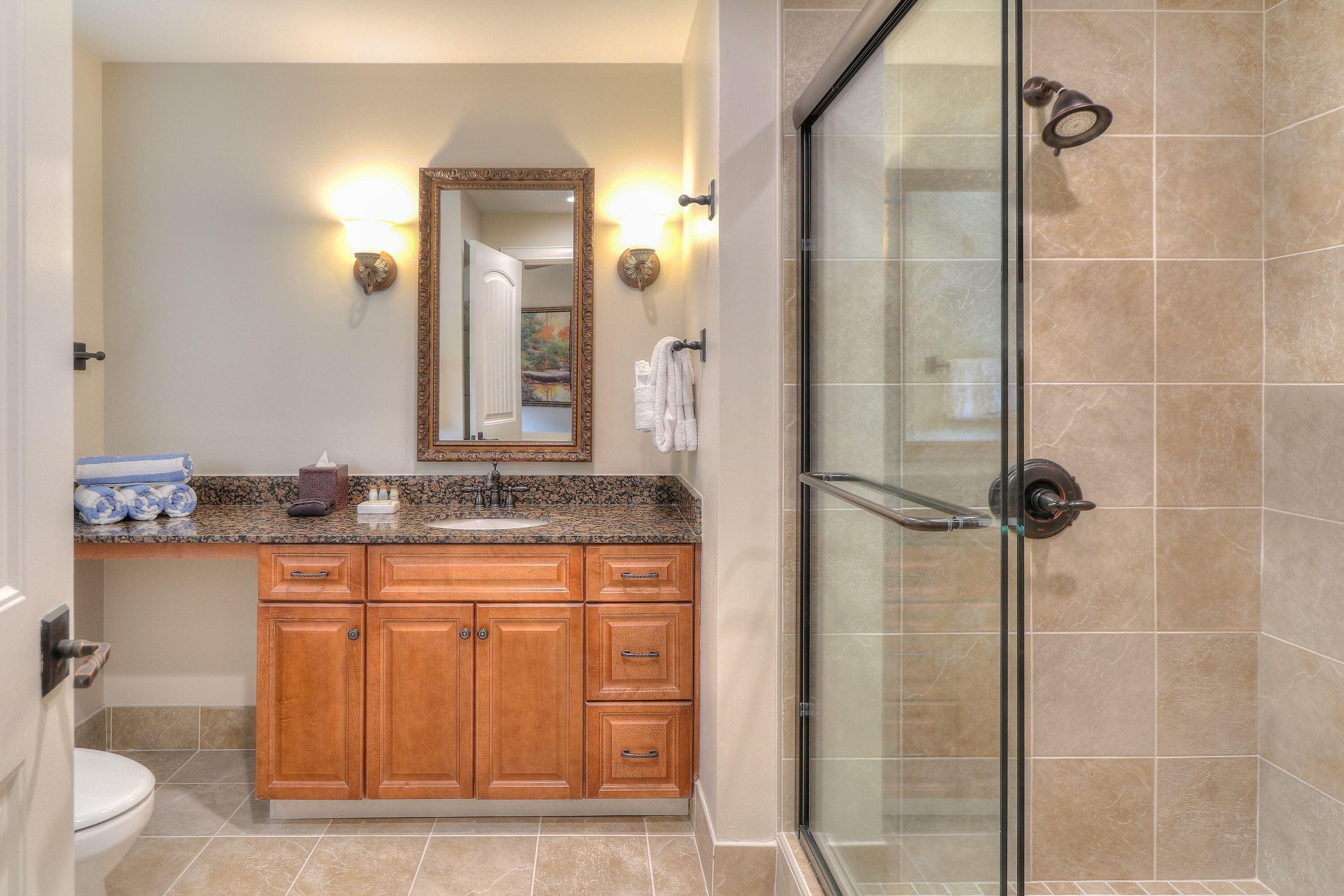 Un baño con tocador de madera, lavamanos, espejo y cabina de ducha de vidrio.