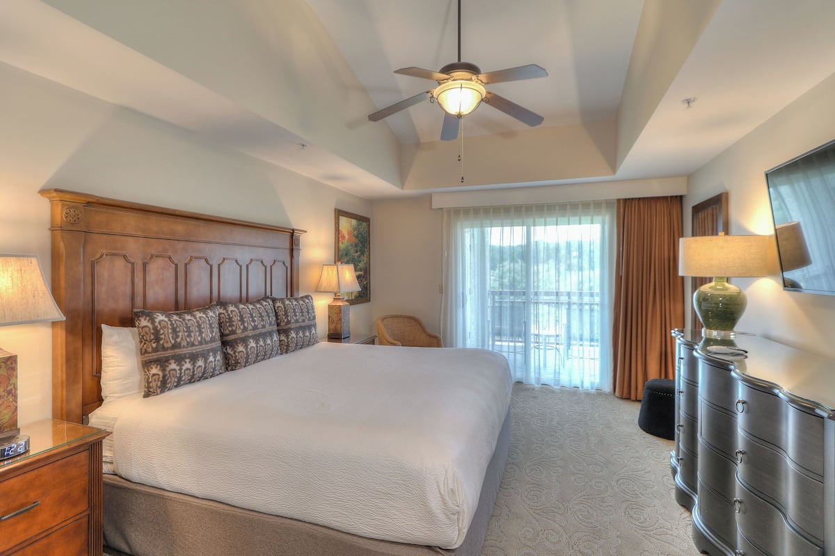 A hotel room with a large bed, a ceiling fan, a dresser, and a window with curtains.