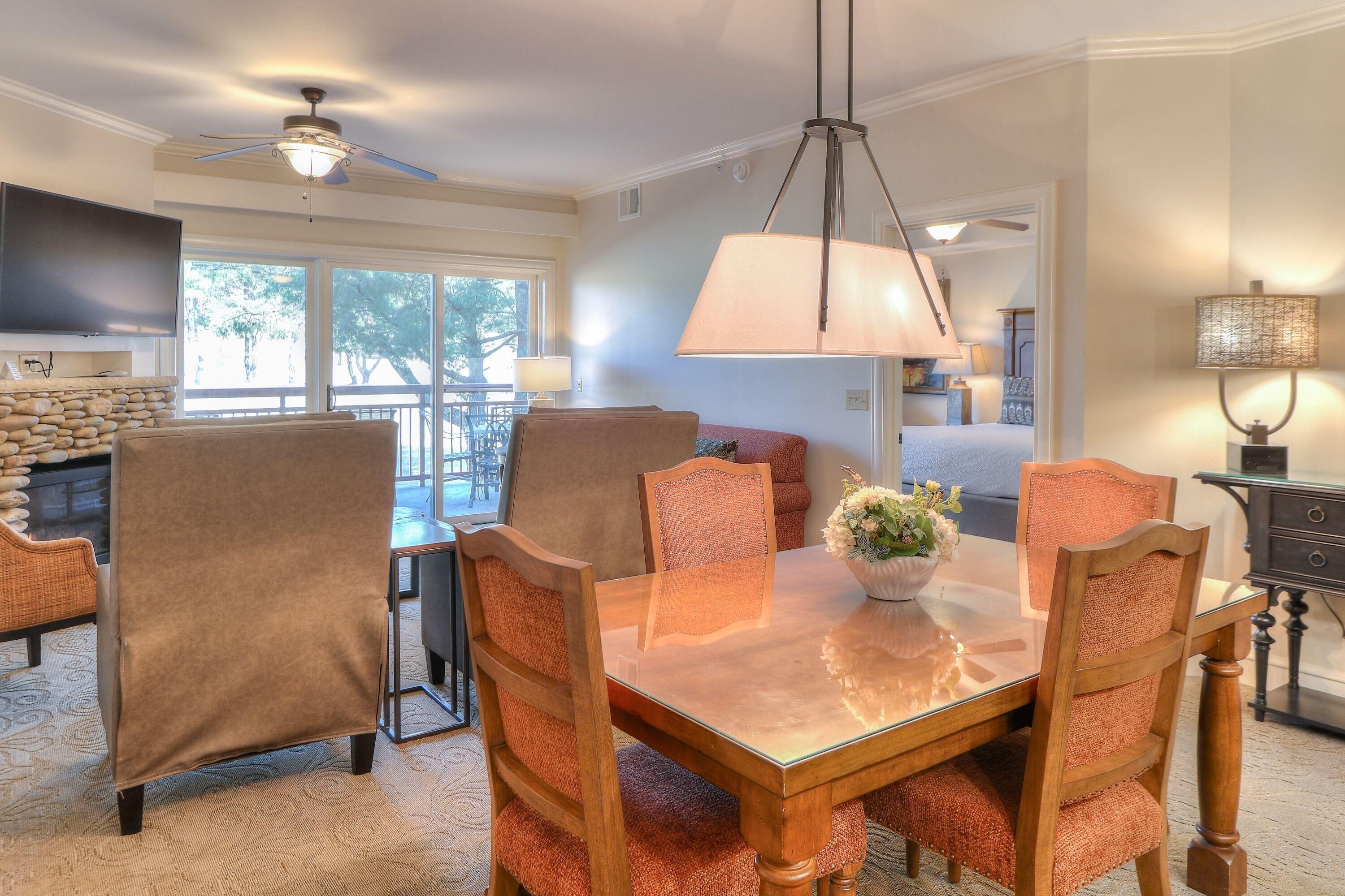 A dining area with a glass table, wooden chairs, and a ceiling fan.