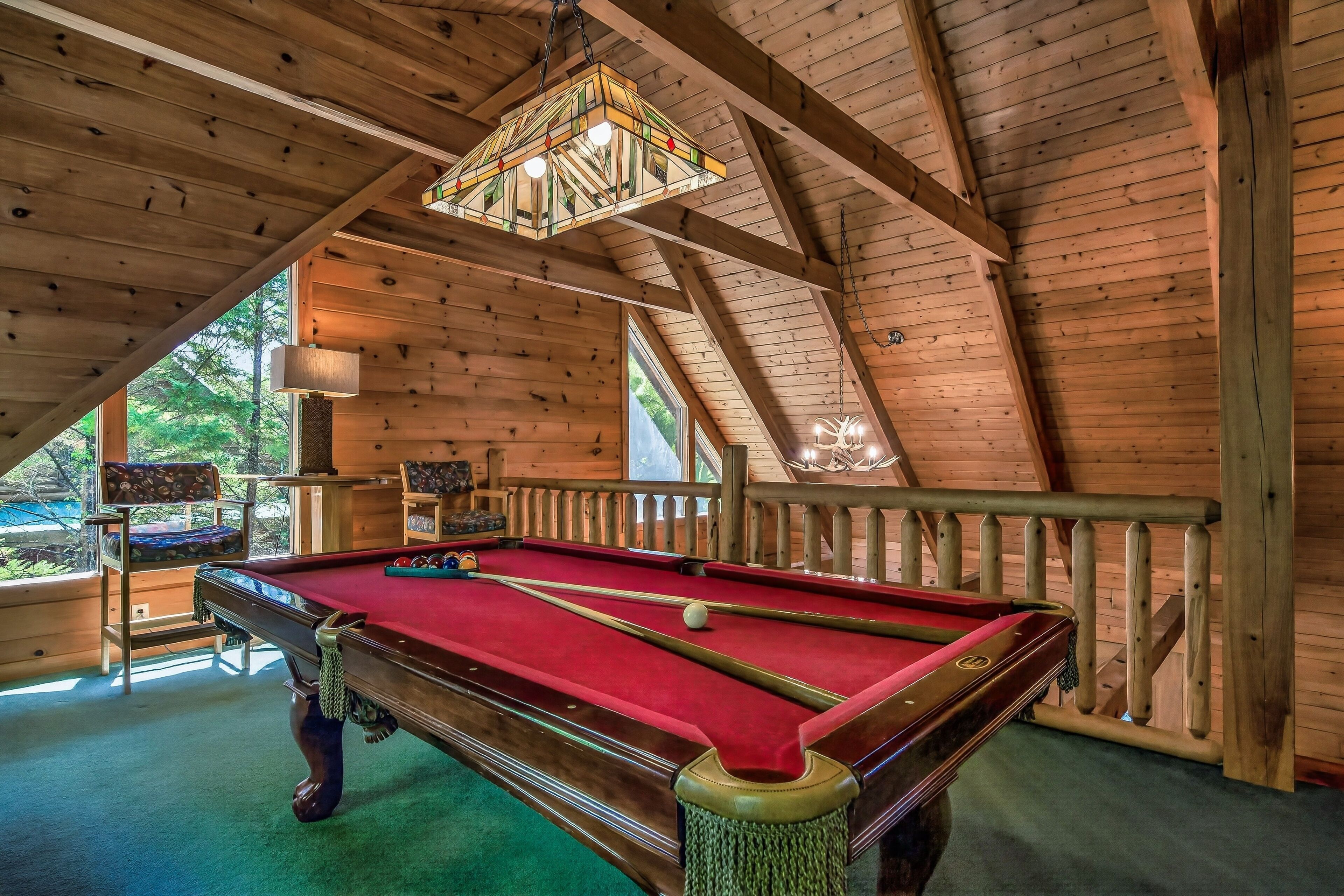 A pool table in a wooden room with a sloped ceiling and a hanging light fixture.